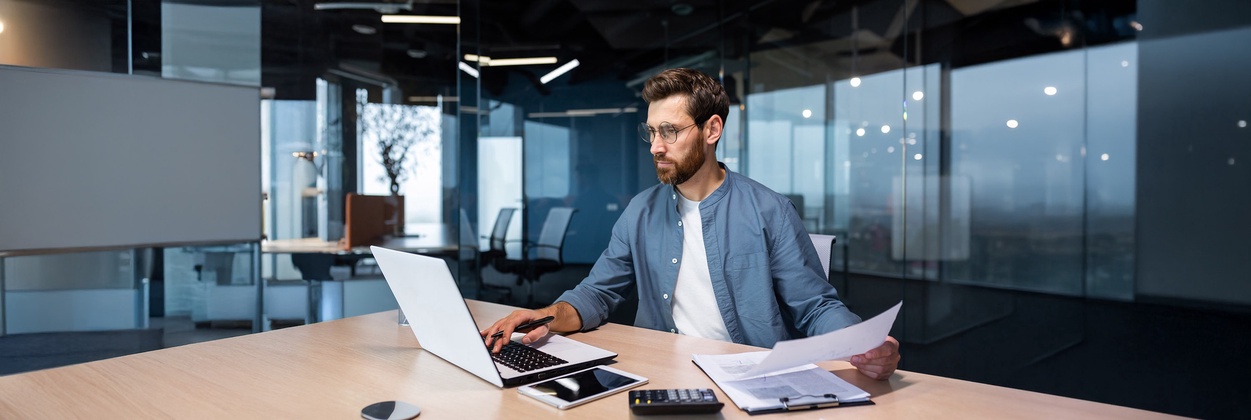 Junger Wirtschaftsprüfer sitzt in einem modernen Büro an seinem Laptop