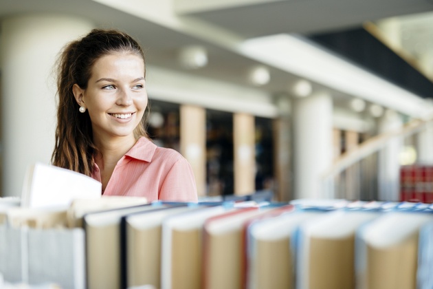 Eine Jurastudentin steht in der Bibiliothek vor einer Reihe von Büchern.