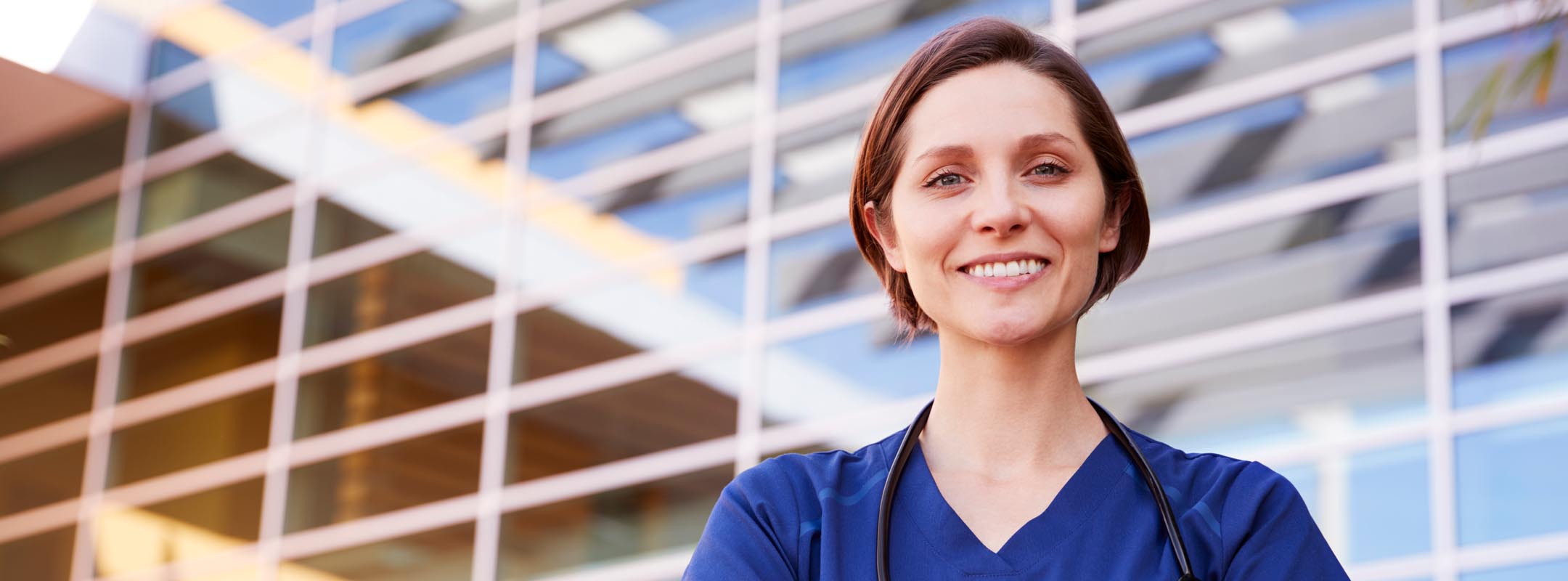 Eine lächelnde Krankenschwester steht vor einem Gebäude.