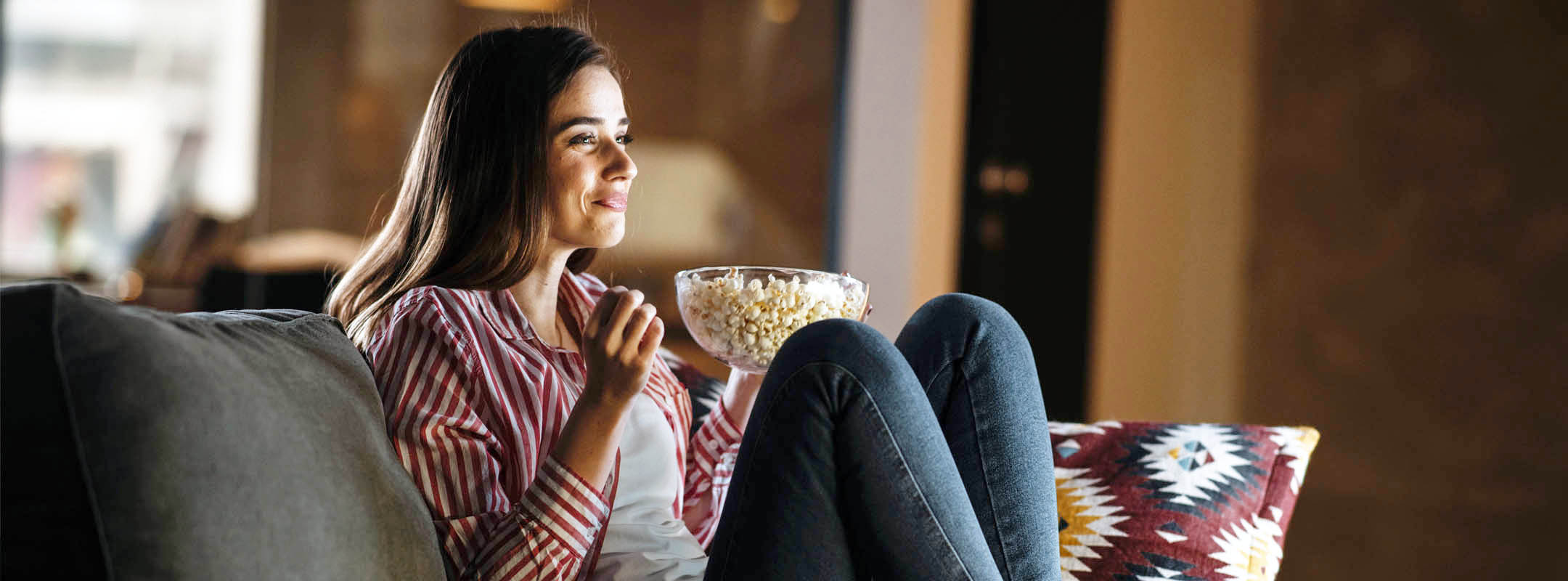 Eine Frau sitzt mit Popcorn auf dem Sofa.