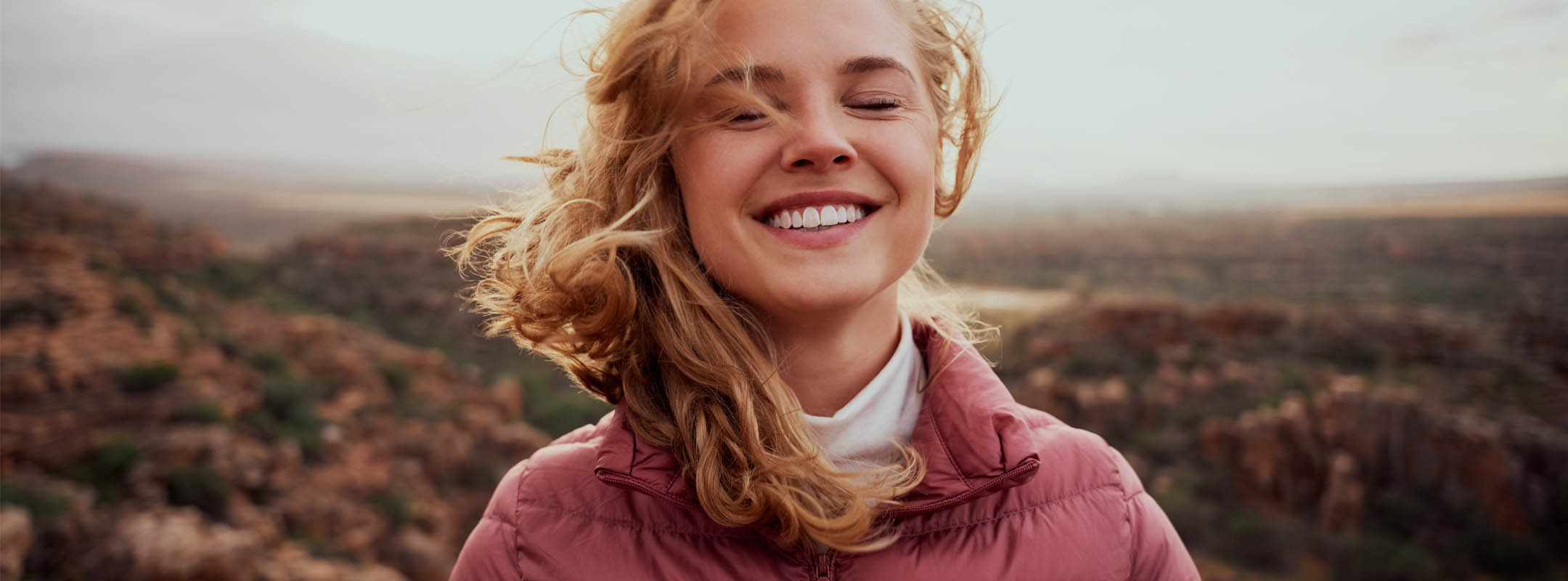 Eine Frau steht mit geschlossenen Augen in der Natur und lacht
