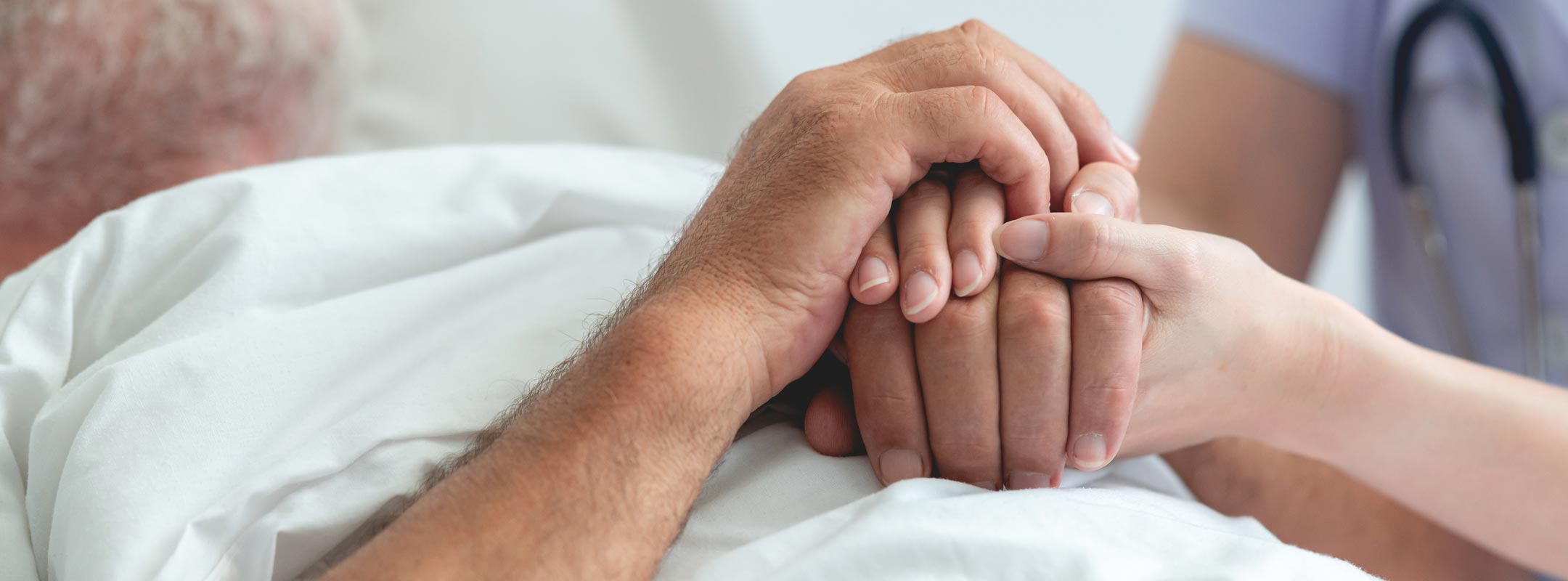 Eine Pflegerin hält die Hände eines alten Manns, der im Bett liegt