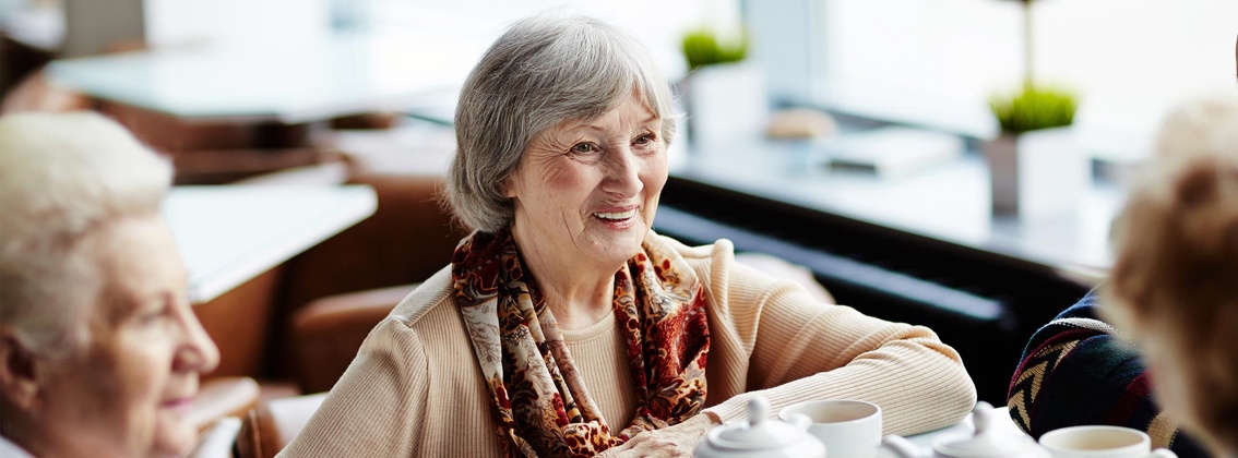Eine alte Frau sitzt mit Freundinnen in einem Café
