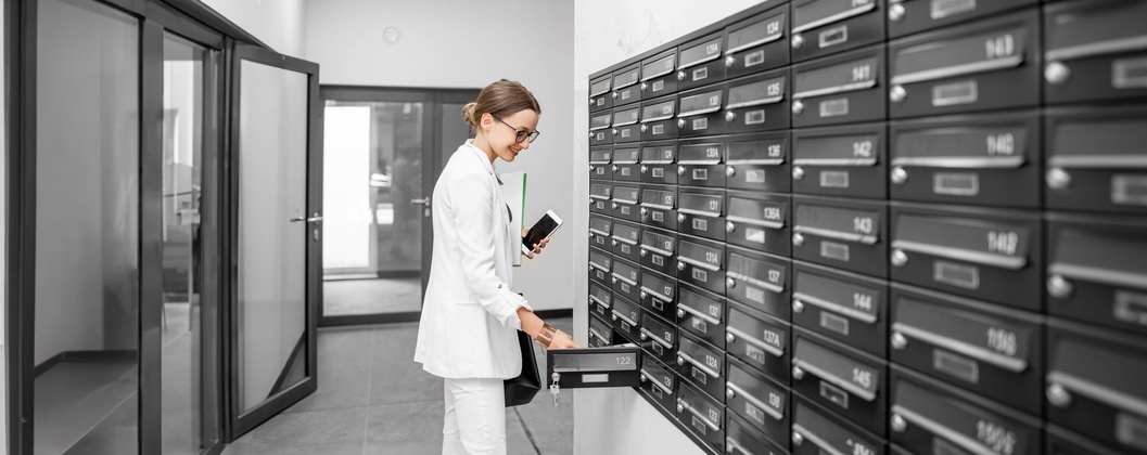 Geschäftsfrau mit Handy öffnet Briefkasten