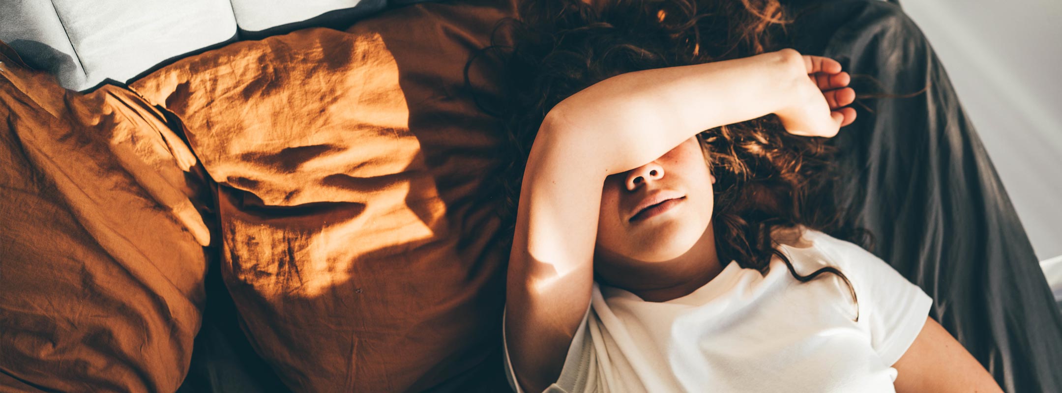Eine Frau liegt im Bett und verdeckt ihre Augen mit dem Arm