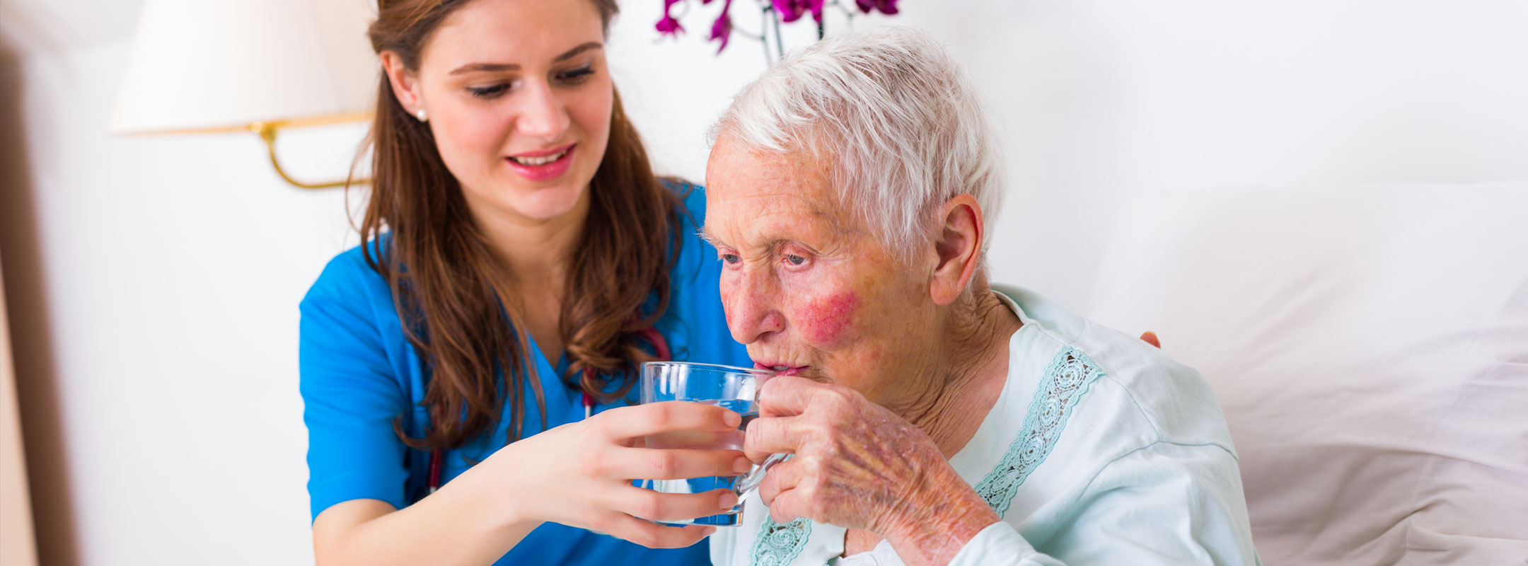 Eine junge Pflegerin gibt einer alten Frau ein Glas Wasser.