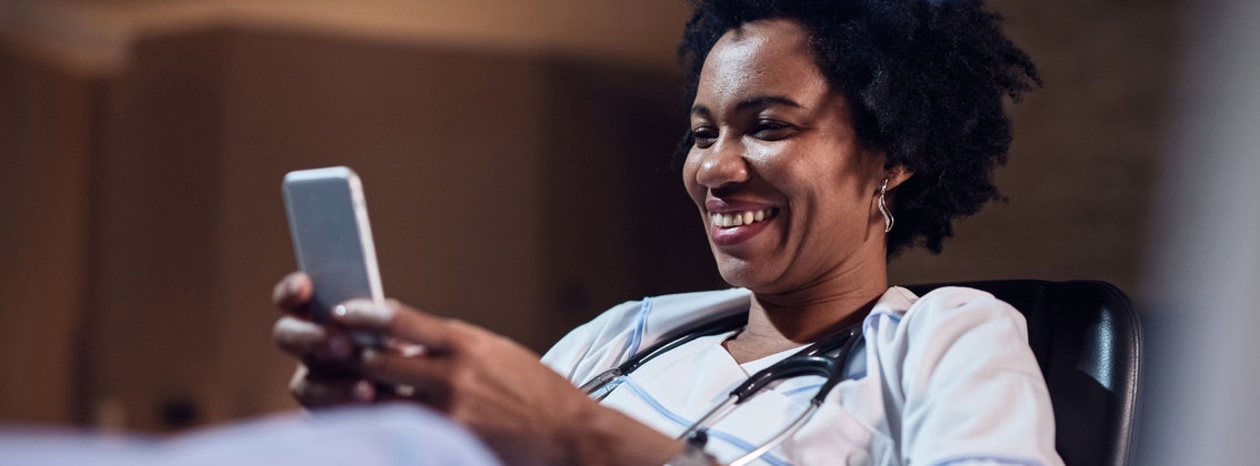 Eine Pflegerin schaut lachend auf ihr Smartphone