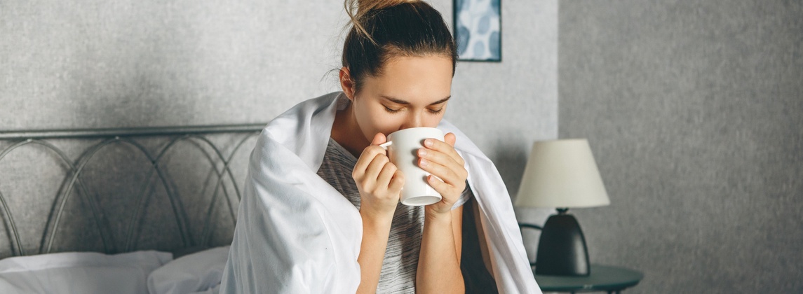 Jura Studentin sitzt krank im Bett und trinkt Tee