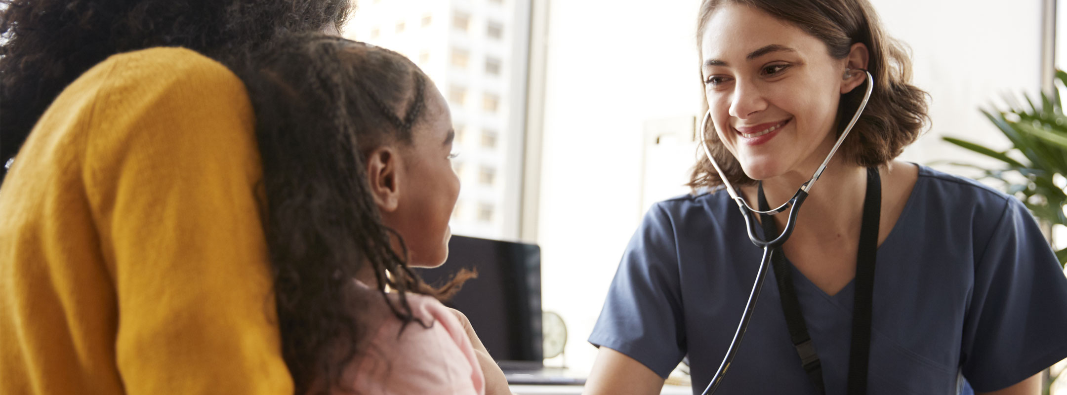 Eine junge Pflegerin hört ein Kind mit einem Stethoskop ab