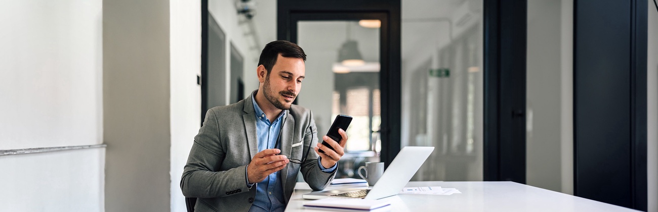 Mann mit Handy am Computer